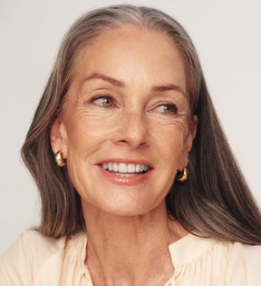 The Valentines Bundle featuring The Soft Tan Bronzer on a smiling model with grey hair for a radiant glow.