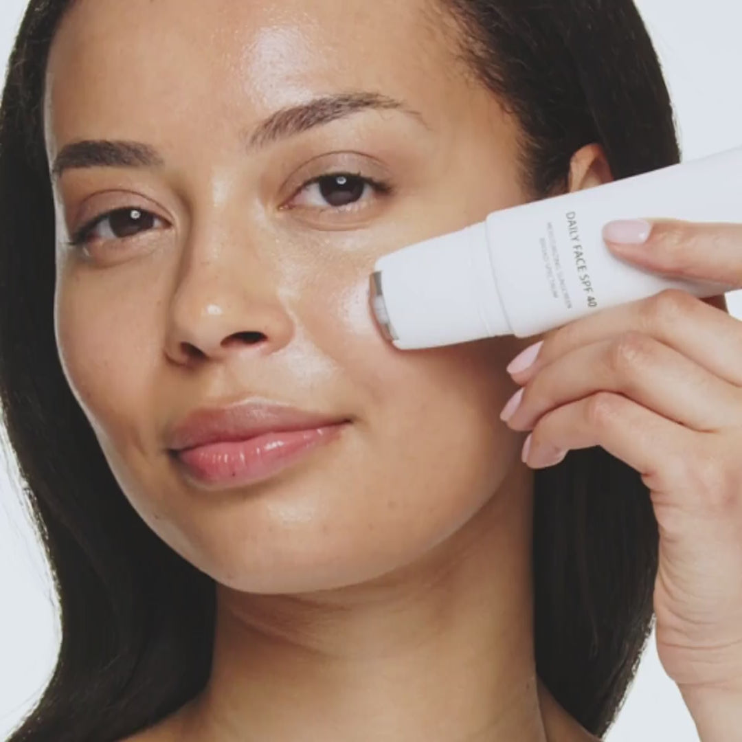 Woman applying Daily Face SPF 40 using the cooling rollerball applicator for a radiant complexion.