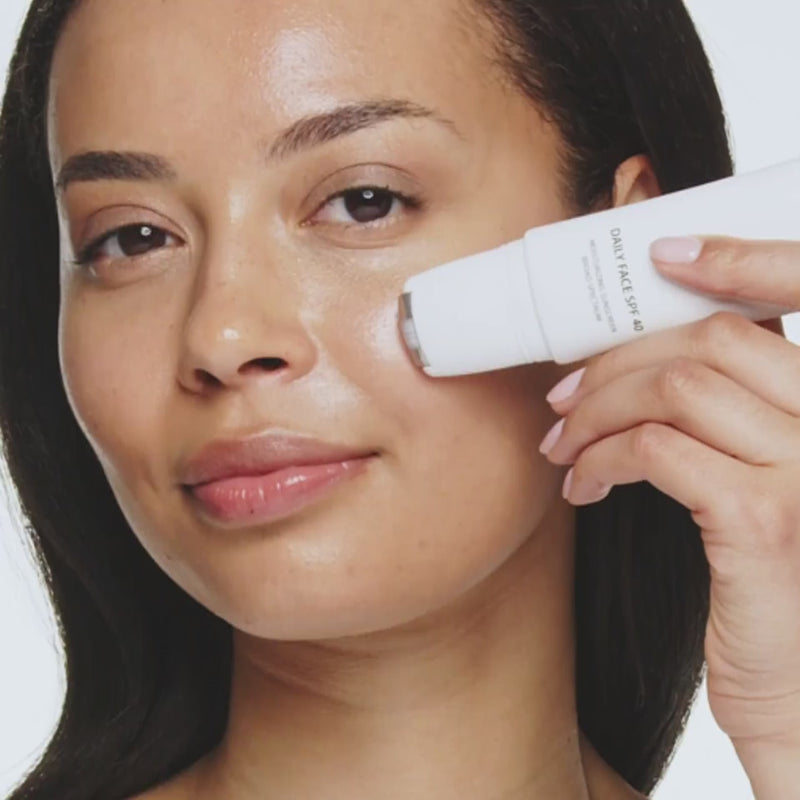 Woman applying Daily Face SPF 40 using the cooling rollerball applicator for a radiant complexion.