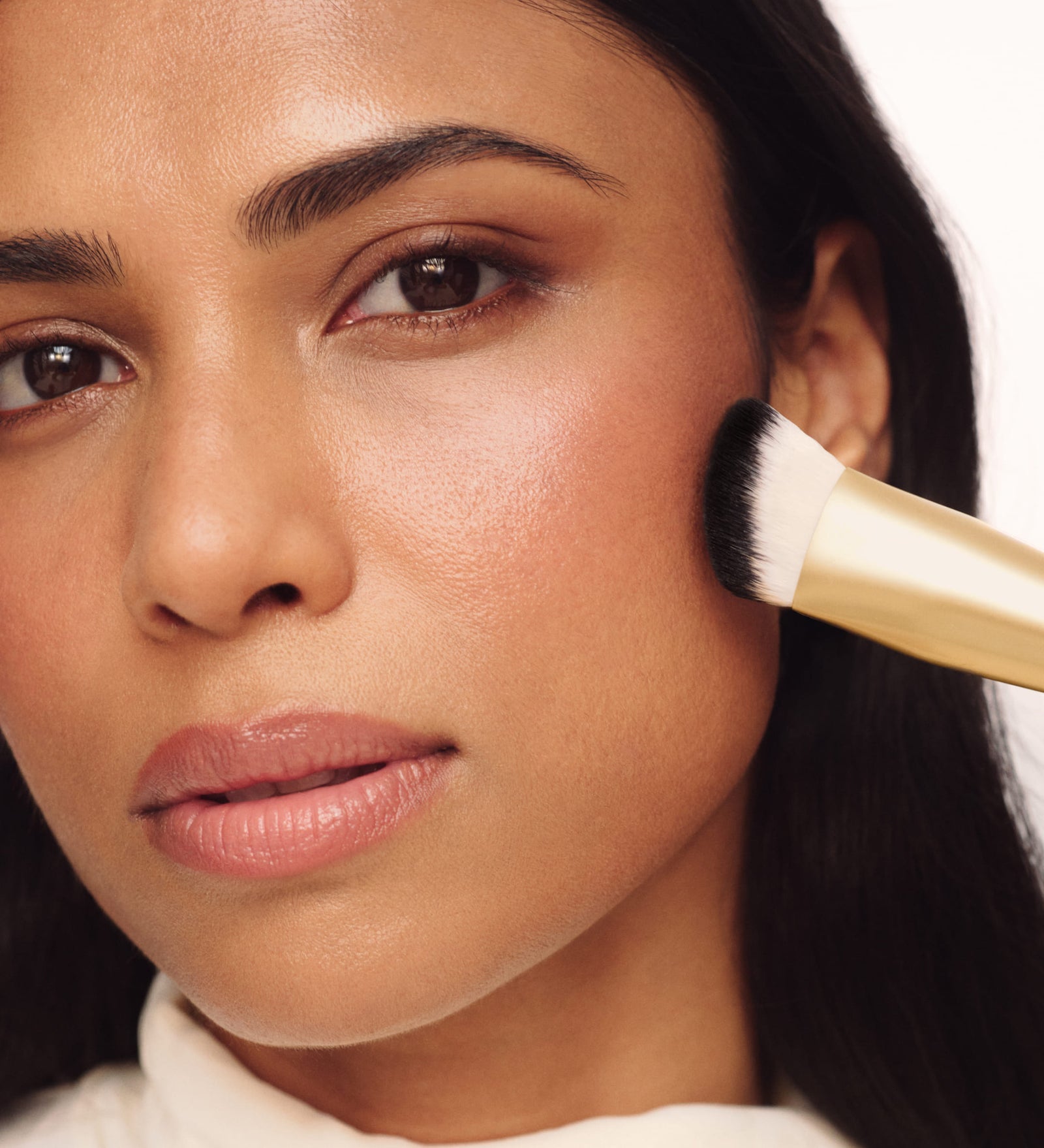 Model blending makeup on her cheek with The Essential Brush for a seamless, airbrushed finish.