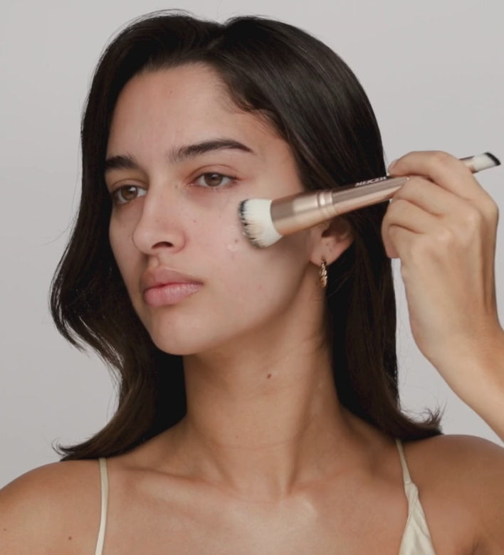 Changing Foundation being blended onto a model's cheek with a makeup brush for a natural glow.